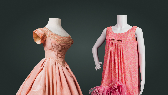 Deux robes roses sont présentées. L’une est une robe de bal formelle à manches courtes des années 1860, l’autre une robe de cocktail courte et sans manches ornée de plumes d’autruche, des années 1960.