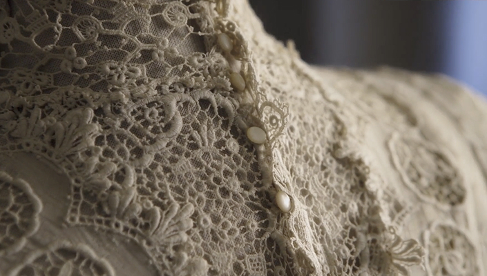 Détails de l’encolure d’une robe de mariée des années 1930, montrant une broderie en dentelle complexe et de petits boutons couleur ivoire.