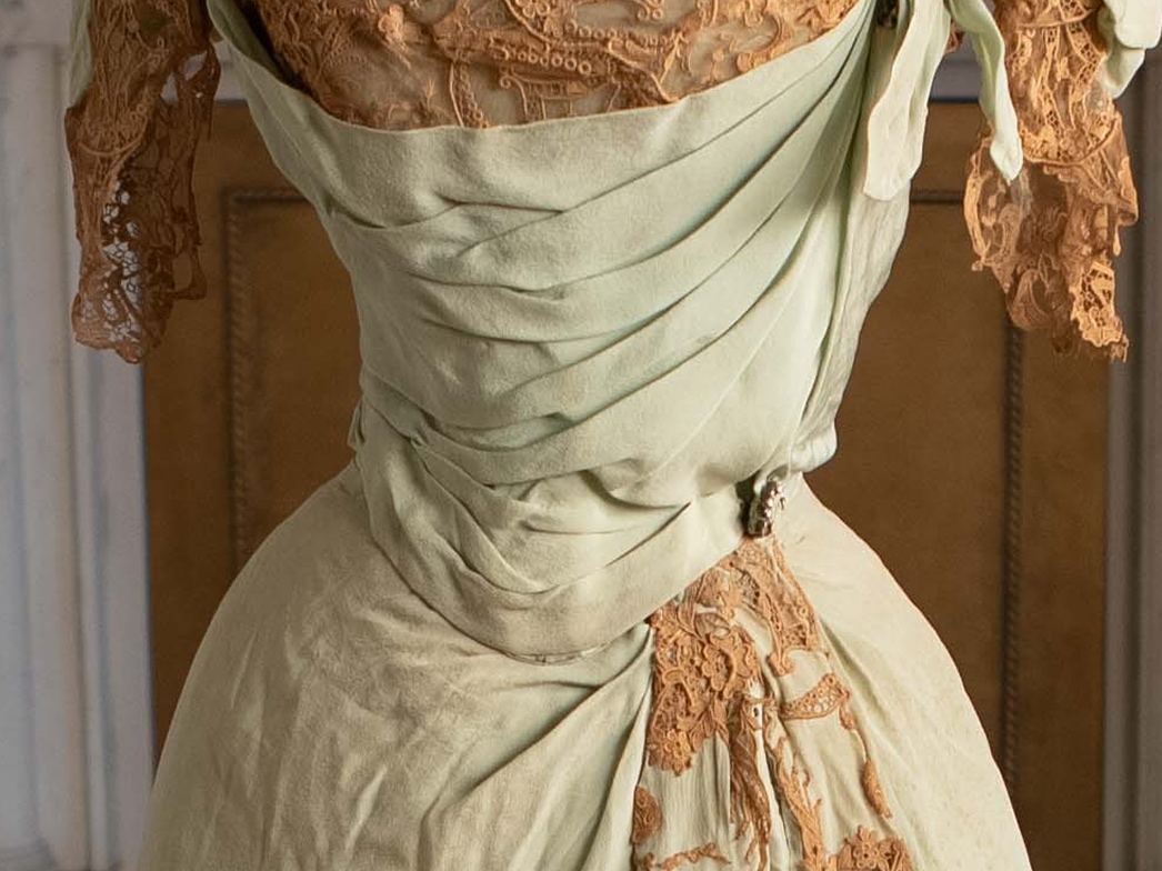 Au milieu d’une robe ornée, une petite broche en strass orne la soie vert pâle pliée.