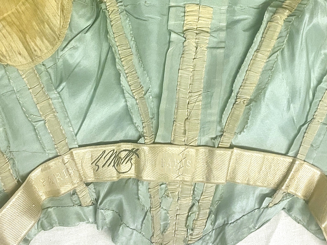 Un gros plan de l’intérieur du corsage d’une robe révèle plusieurs baleines menant à une ceinture intérieure portant l’insigne de la marque Worth.