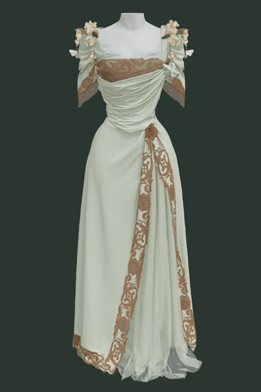 Vue de face d’une représentation 3D de la robe Worth, montrant sa jupe et son corsage vert menthe séparés, ornés de dentelle de coton et de fleurs de liseron. L’encolure est en tulle de soie et dentelle de 7,5 cm de large à bord irrégulier. La dentelle est également doublée sur le corsage pour accentuer l’ampleur. Un drapé asymétrique en crêpe de Chine de soie recouvre le corsage et la jupe, se détachant harmonieusement sur la base structurée du vêtement.