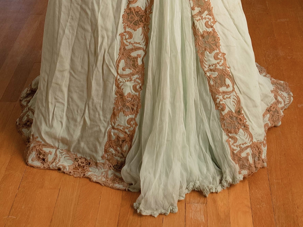 Le bas d’une robe en soie présente un empiècement en tissu transparent, orné d’appliqués de dentelle sur les bords.
