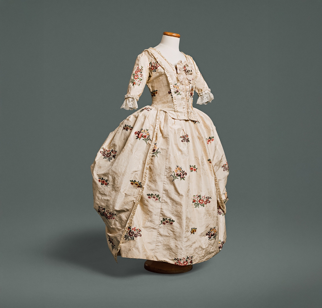 Une robe en soie blanche ornée de fleurs sur fond blanc, avec un corsage ajusté devant et derrière et une taille marquée par une couture.