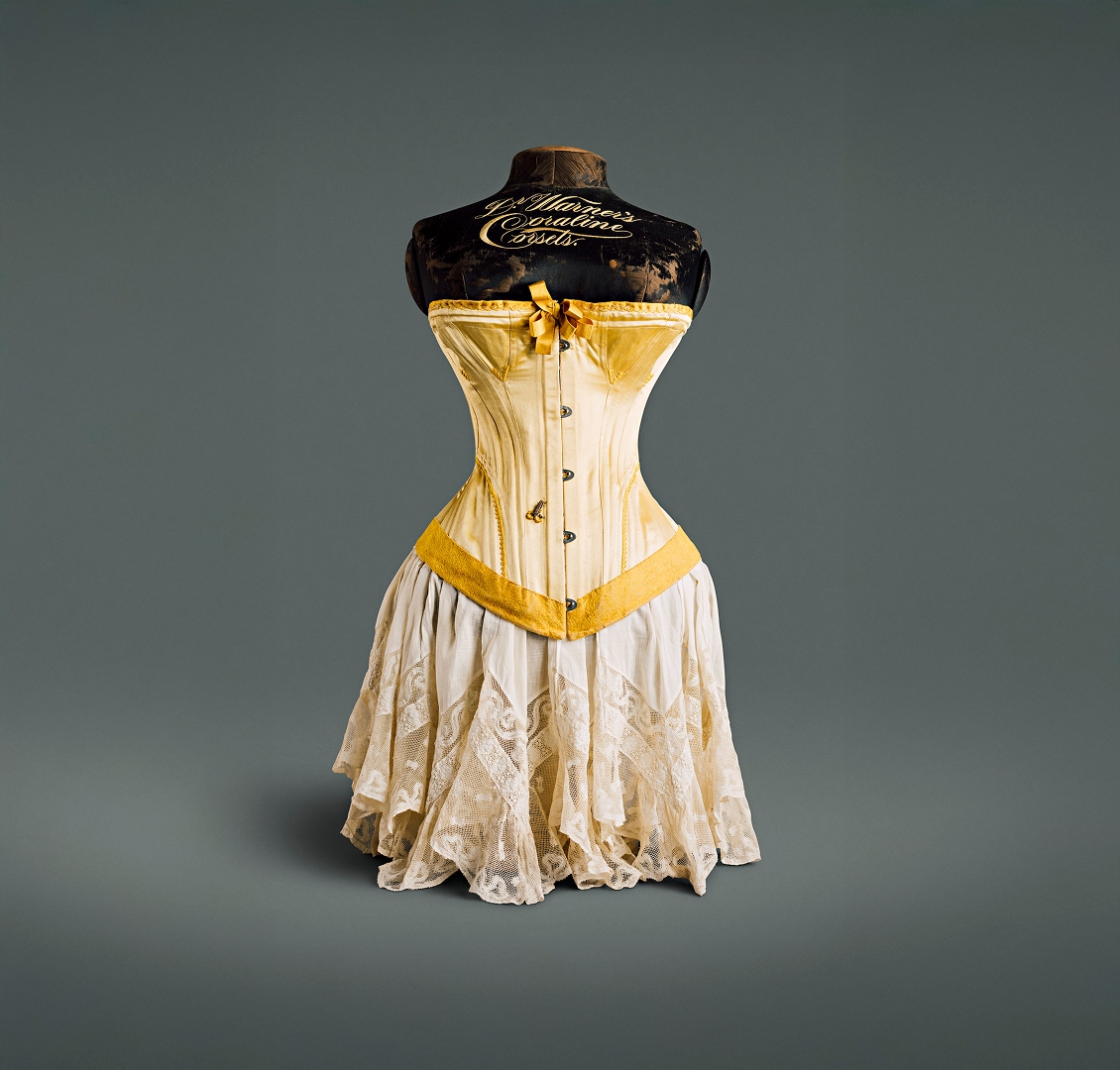 Un corset en soie jaune canari avec un nœud au niveau de la poitrine, un ourlet en velours et des crochets de fermeture en métal.