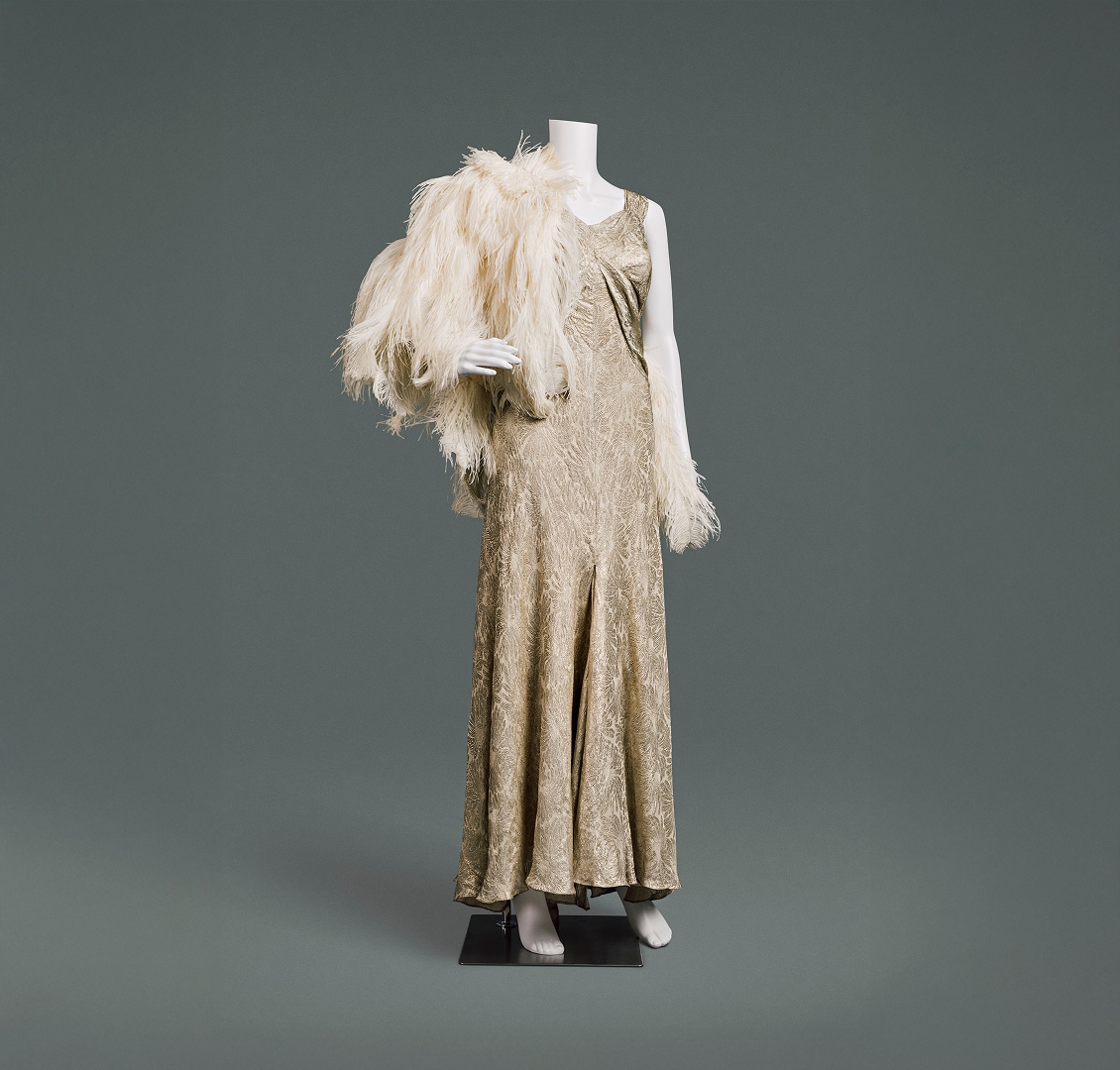 Une robe de soirée glamour sans manches en lamé de soie à motifs dorés, avec une cape de plumes.