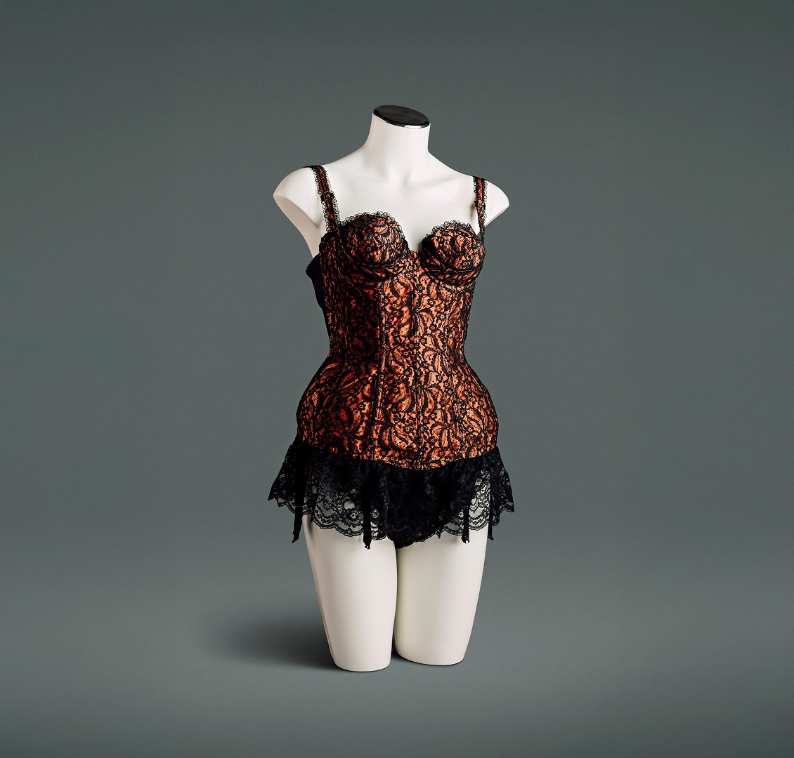 Un bustier en satin de nylon avec superposition de dentelle noire est doté d’un soutien-gorge conique à coutures circulaires avec armature sous le bonnet, de panneaux élastiques en maille power mesh sur les côtés et dans le dos, d’un volant en dentelle profond et de jarretières intégrées.