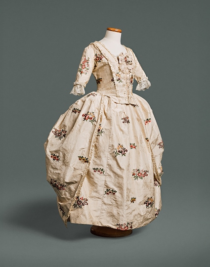 Une robe en soie blanche ornée de fleurs sur fond blanc, avec un corsage ajusté devant et derrière et une taille marquée par une couture.