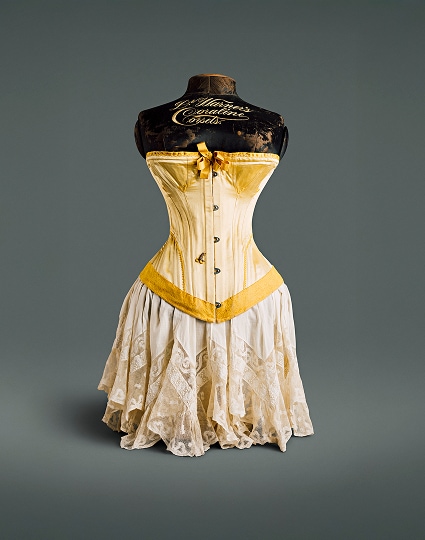Un corset en soie jaune canari avec un nœud au niveau de la poitrine, un ourlet en velours et des crochets de fermeture en métal.