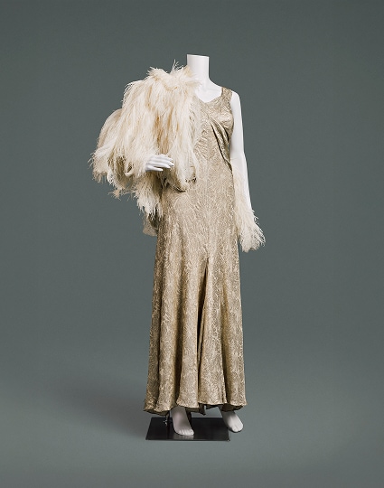 Une robe de soirée glamour sans manches en lamé de soie à motifs dorés, avec une cape de plumes.