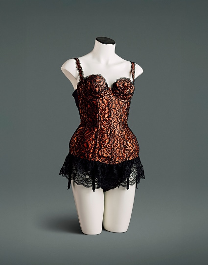 Un bustier en satin de nylon avec superposition de dentelle noire est doté d’un soutien-gorge conique à coutures circulaires avec armature sous le bonnet, de panneaux élastiques en maille power mesh sur les côtés et dans le dos, d’un volant en dentelle profond et de jarretières intégrées.