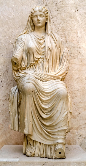 Statue antique en marbre d’une impératrice romaine assise, vêtue d’une robe fluide. La statue est endommagée : il lui manque l’avant-bras droit.