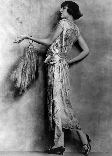 Une garçonne des années 1920, vêtue d’une robe en satin, prend une pose gracieuse.
