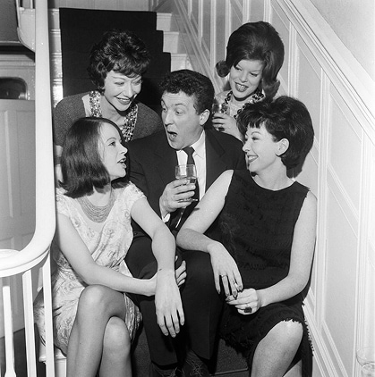 Un célibataire convoité est assis sur les marches, un verre à la main, entouré de quatre belles femmes.