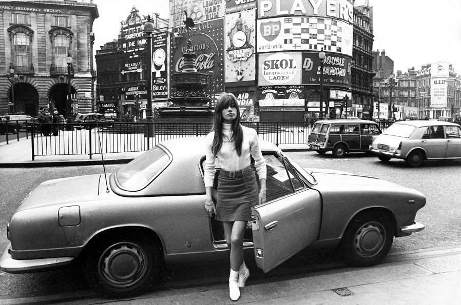 La chanteuse et actrice française Françoise Hardy est descendue d’une voiture de sport vêtue d’un pull à col roulé, d’une minijupe et de bottes en cuir blanc, sur la place Piccadilly à Londres.