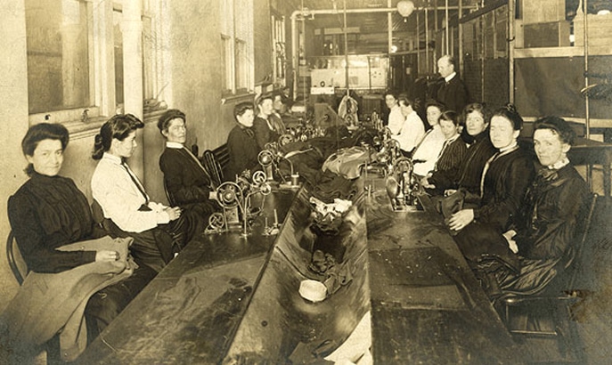 Une longue table avec des couturières travaillant des deux côtés.