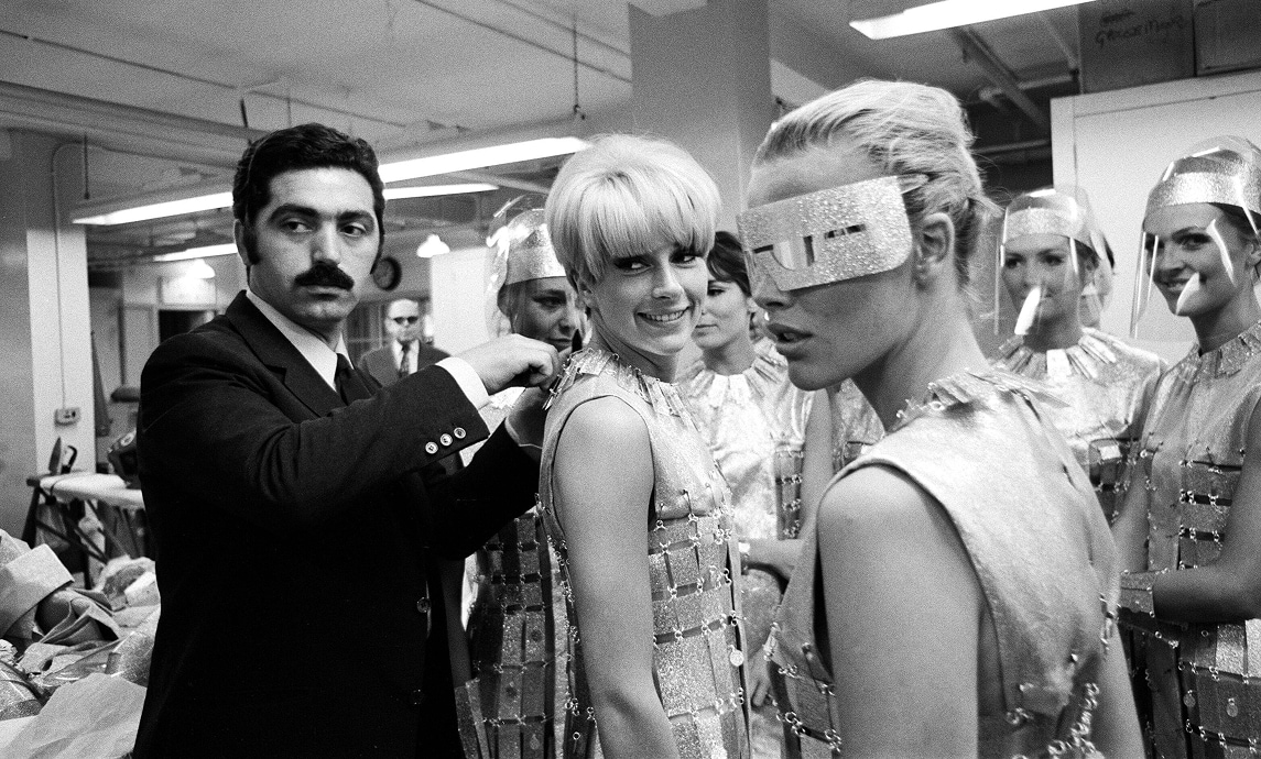 Paco Rabanne, entouré d’actrices portant ses créations futuristes, ajuste le décolleté d’une des tenues.
