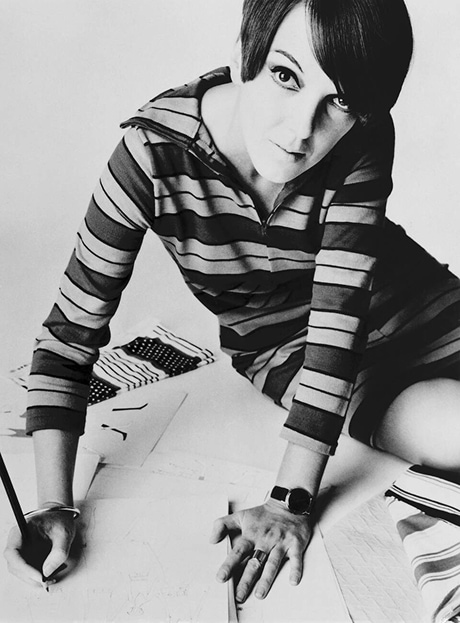 Mary Quant est assise au bord d’une table et dessine des croquis.