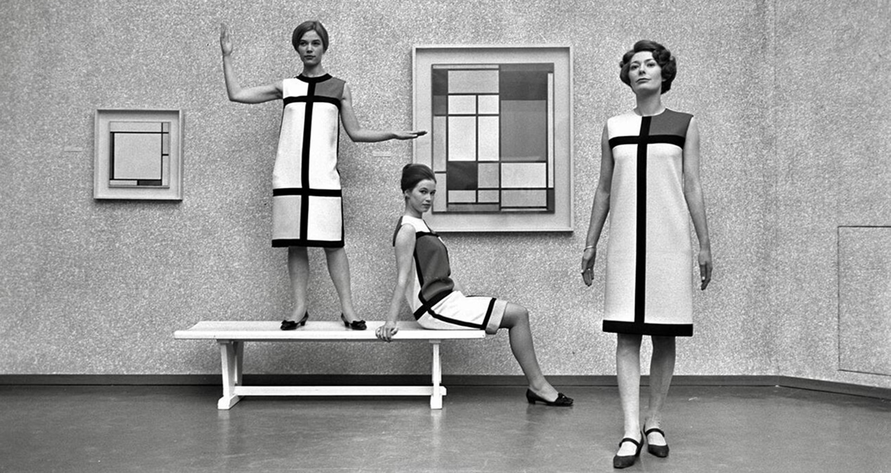 Trois femmes présentent des robes à imprimé Mondrian dans une galerie d’art exposant les peintures de l’artiste.