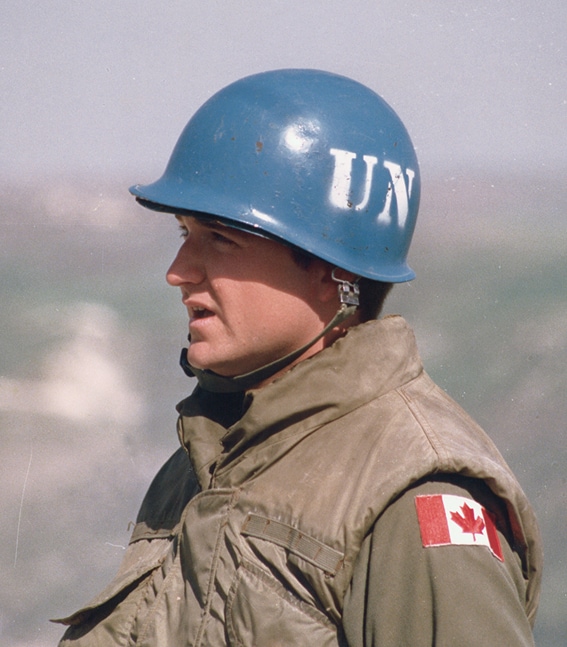 Un soldat canadien de la paix porte un uniforme militaire et un casque bleu sur lequel est inscrit « UN ».