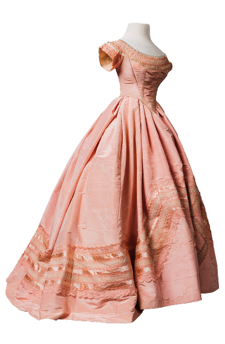 Une robe de soirée rose pâle des années 1860, probablement de fabrication italienne. Elle présente un corsage ajusté à décolleté plongeant et manches courtes. La jupe ample et triangulaire est composée de panneaux en forme de coin plutôt que carrés, ce qui lui confère un volume généreux à l’ourlet tout en affinant la taille.
